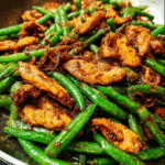 Finished chicken green bean stir fry recipe served over rice with sesame seeds and green onions