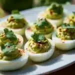 Avocado deviled eggs served on a platter with fresh herbs.