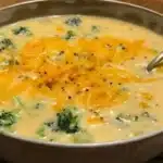 Bowl of creamy broccoli cheddar soup topped with shredded cheese and croutons